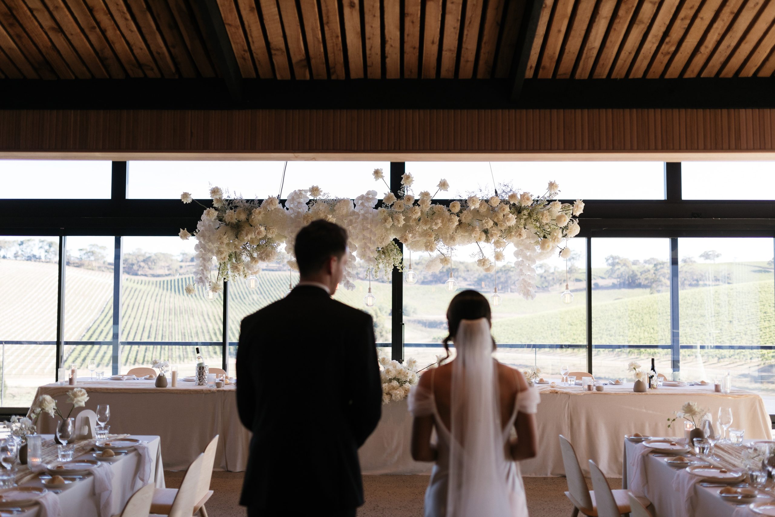 Couple looking at white floral hanging installation, longview vineyard reception space styled by The Modern Approach and Photography Jack Small