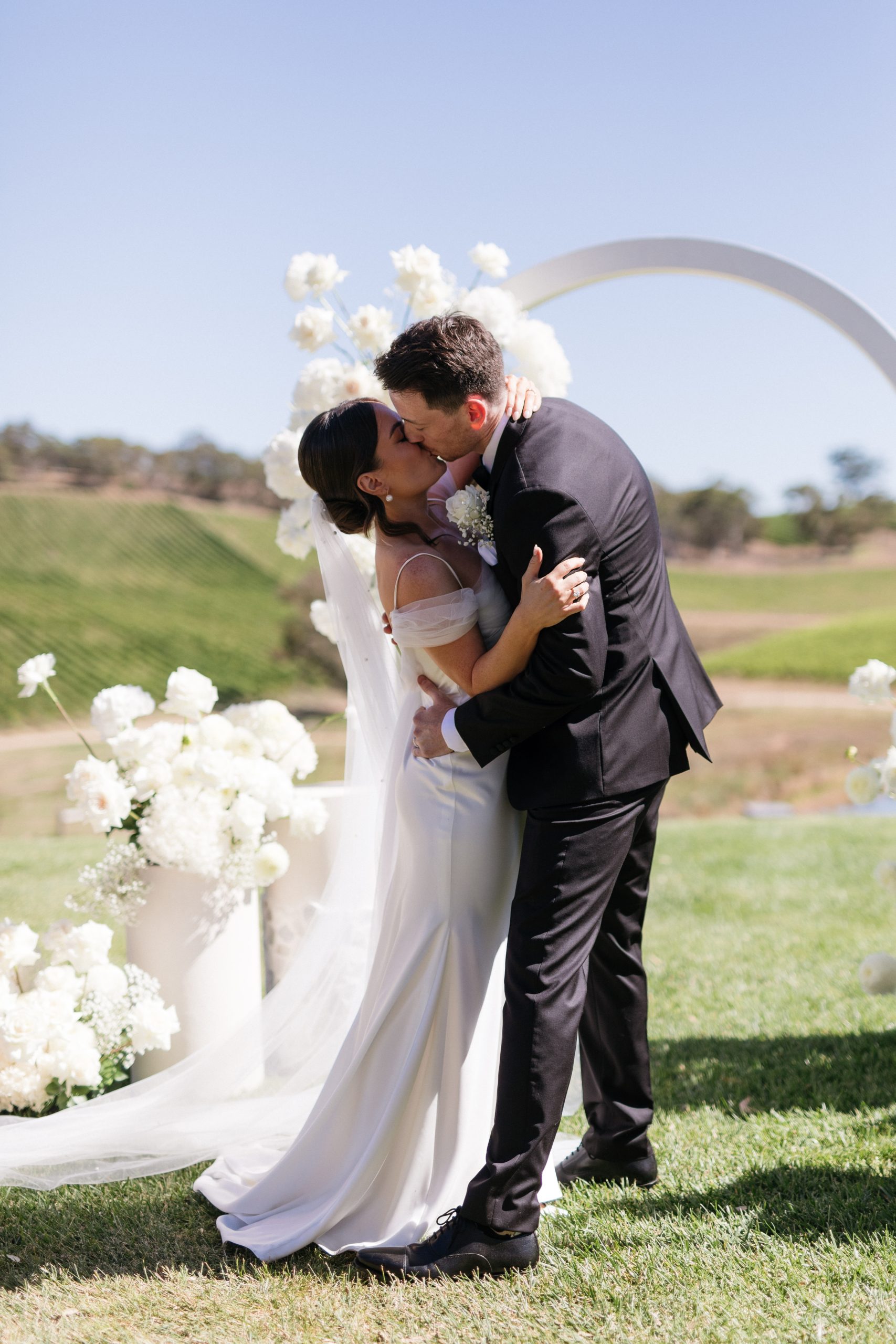Close up of wedding kiss in front of The modern approach white arch wedding arbor, Jack Small Photography