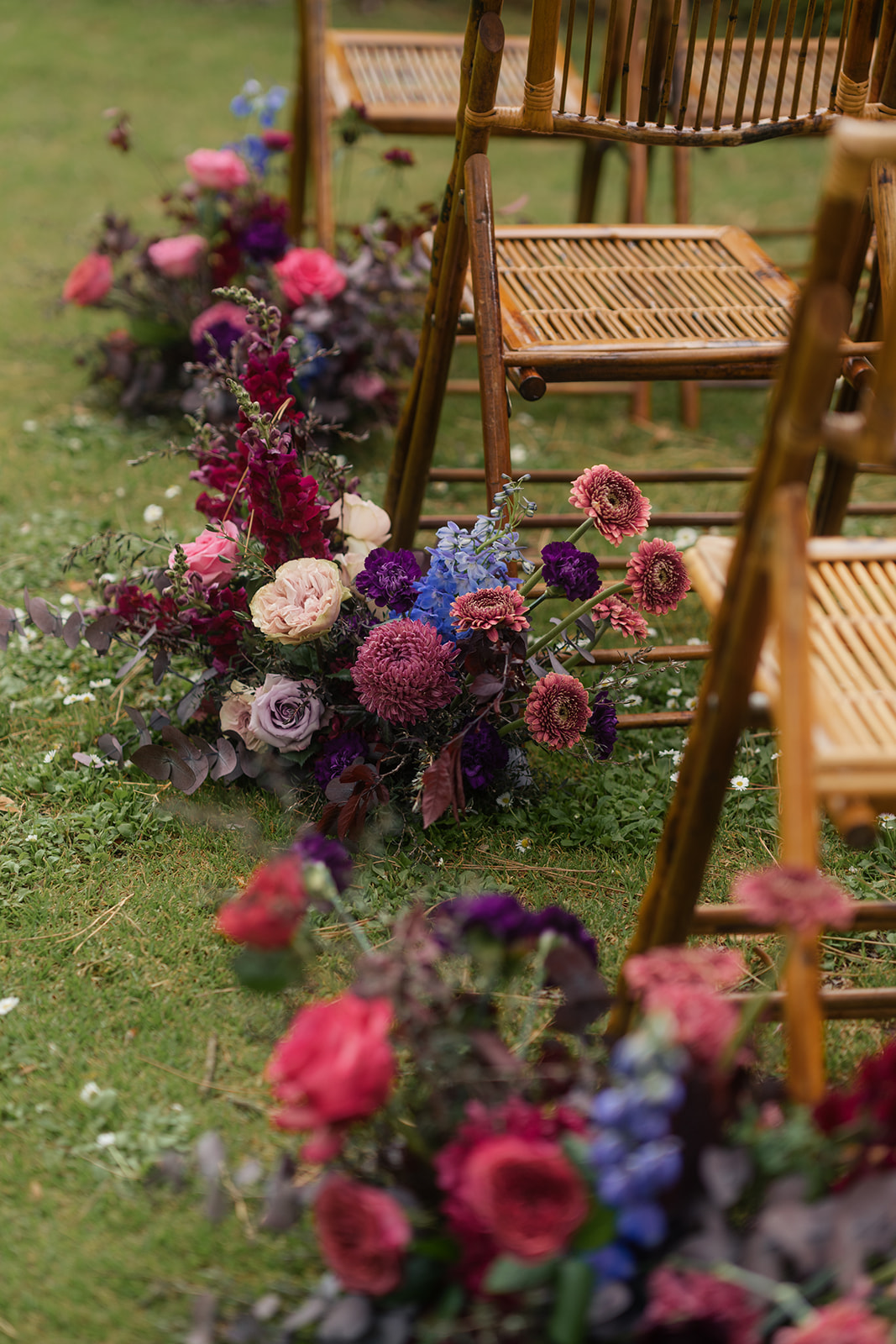 Etherial Botanica wedding florals in dark purple and pink tones lined up along chairs down the wedding aisle to suit the couples moody rustic elegance brief