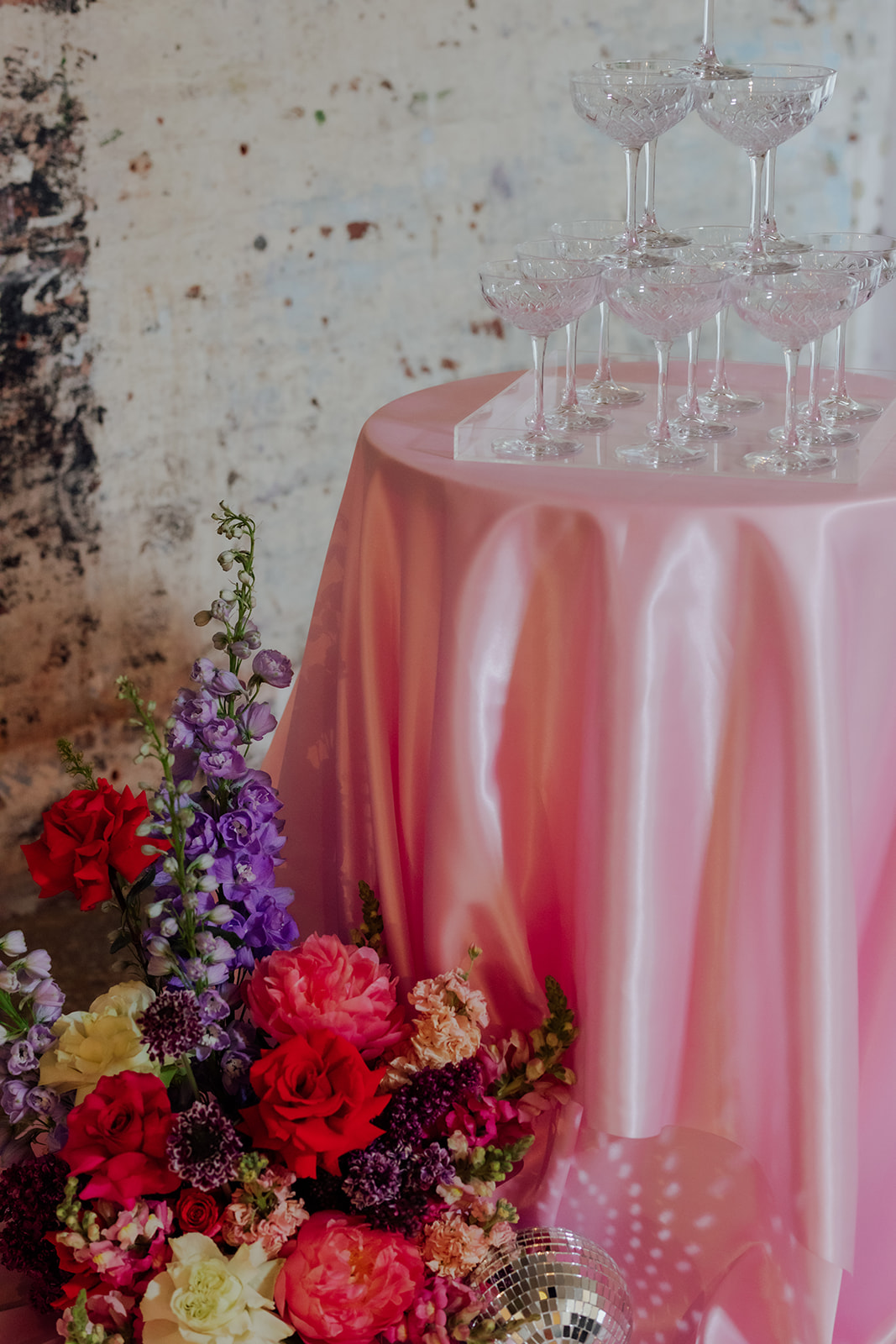 Champagne tower styled to suit Intimate wedding infused with fun and colour using pink satin table cloth, disco ball and colourful flowers