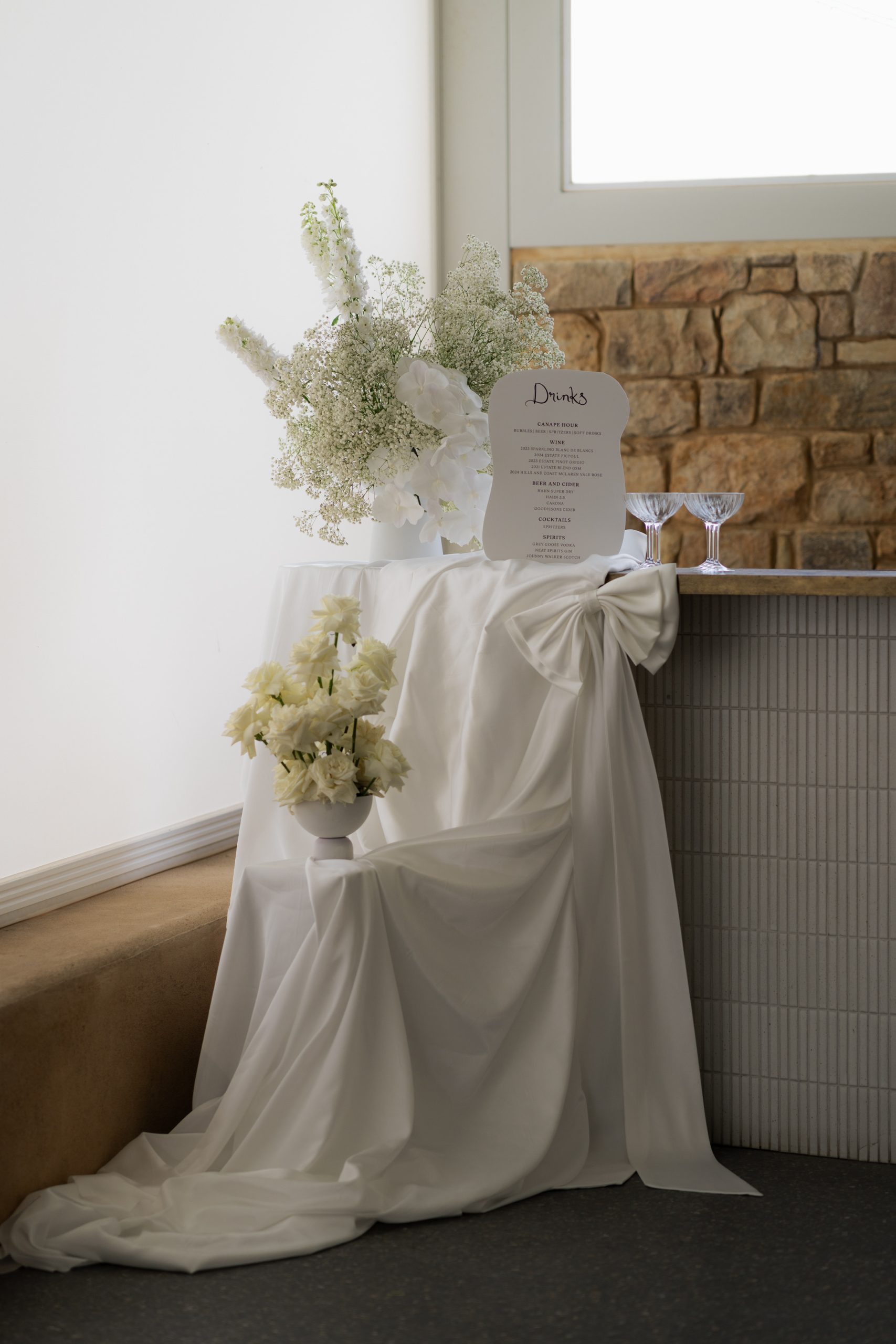 Classic blackened white wedding bar styling with draped fabric, bows and flowers