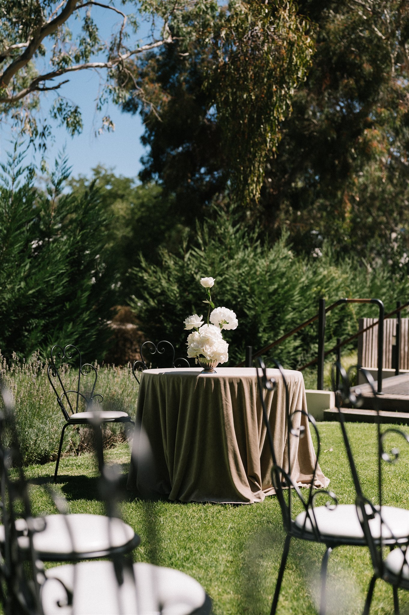 Garden wedding reception at House on Haines witth round tables draped in fabric, white and green florwals and timeless and elegant wrought iron chairs
