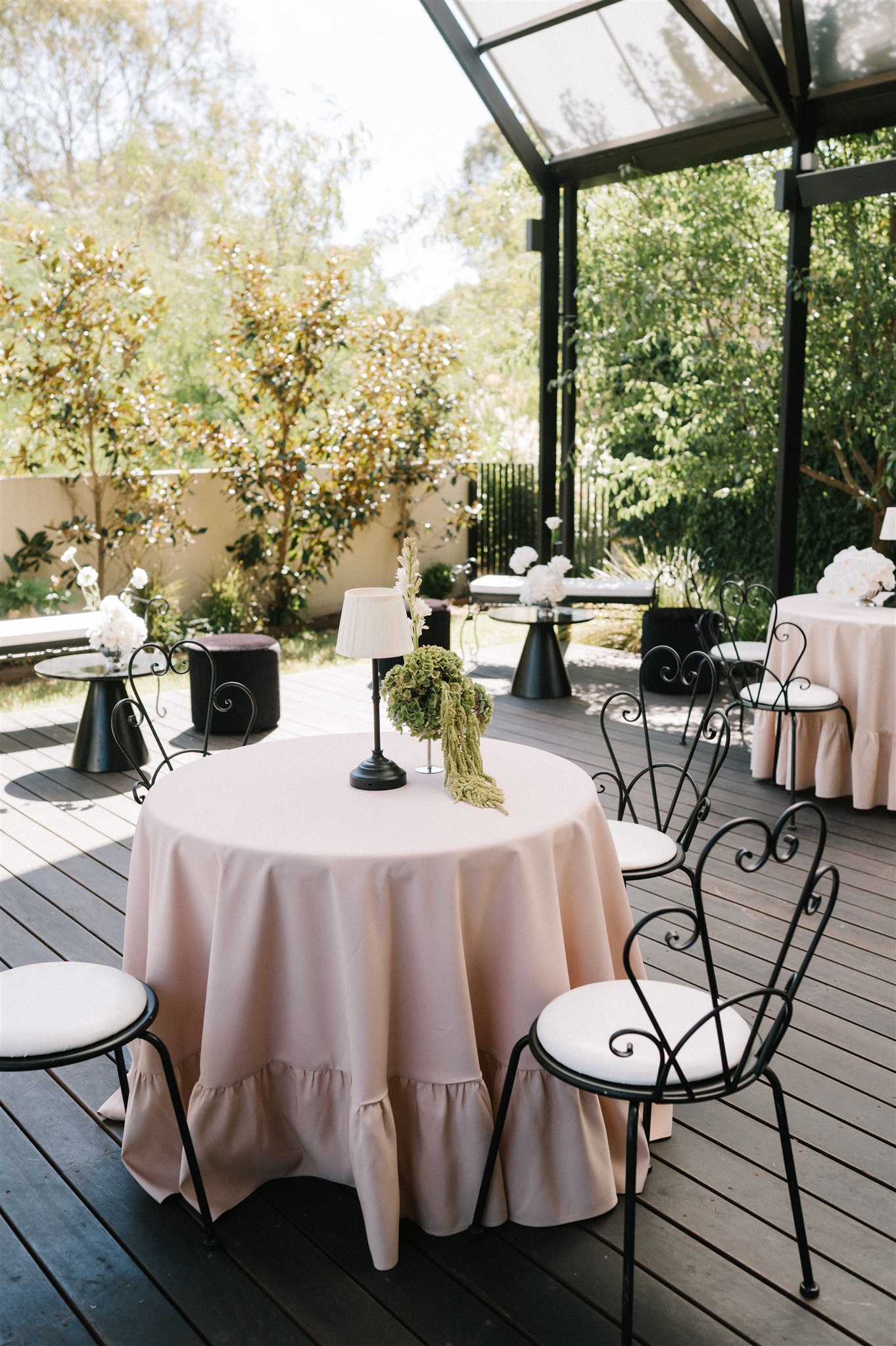 Garden wedding reception with small round tables and wrought iron chairs draped in fabric