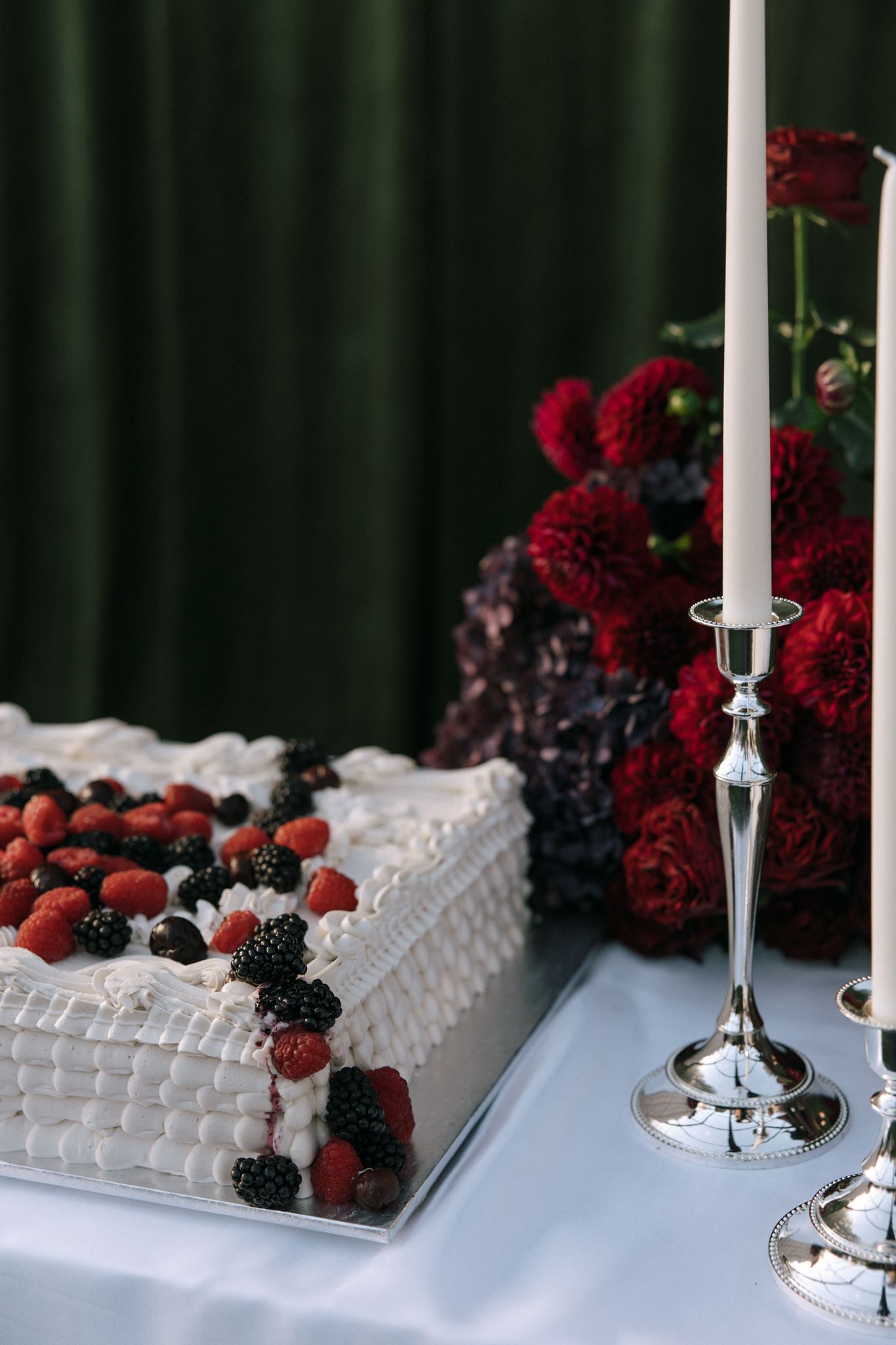 Wedding cake and silver candle holders displayed on silk with berries and dark red wedding flowers