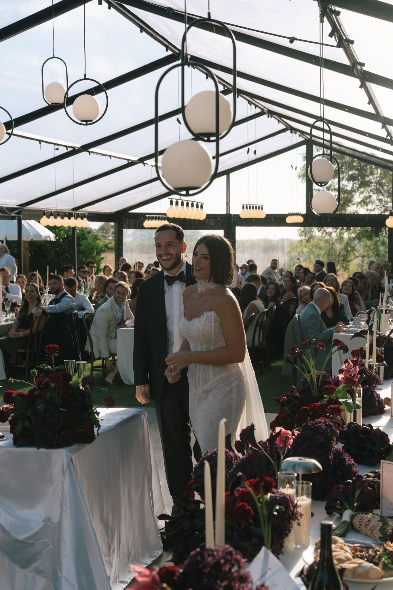 Bride and groom walking through tables at wedding reception in clear roof marquee