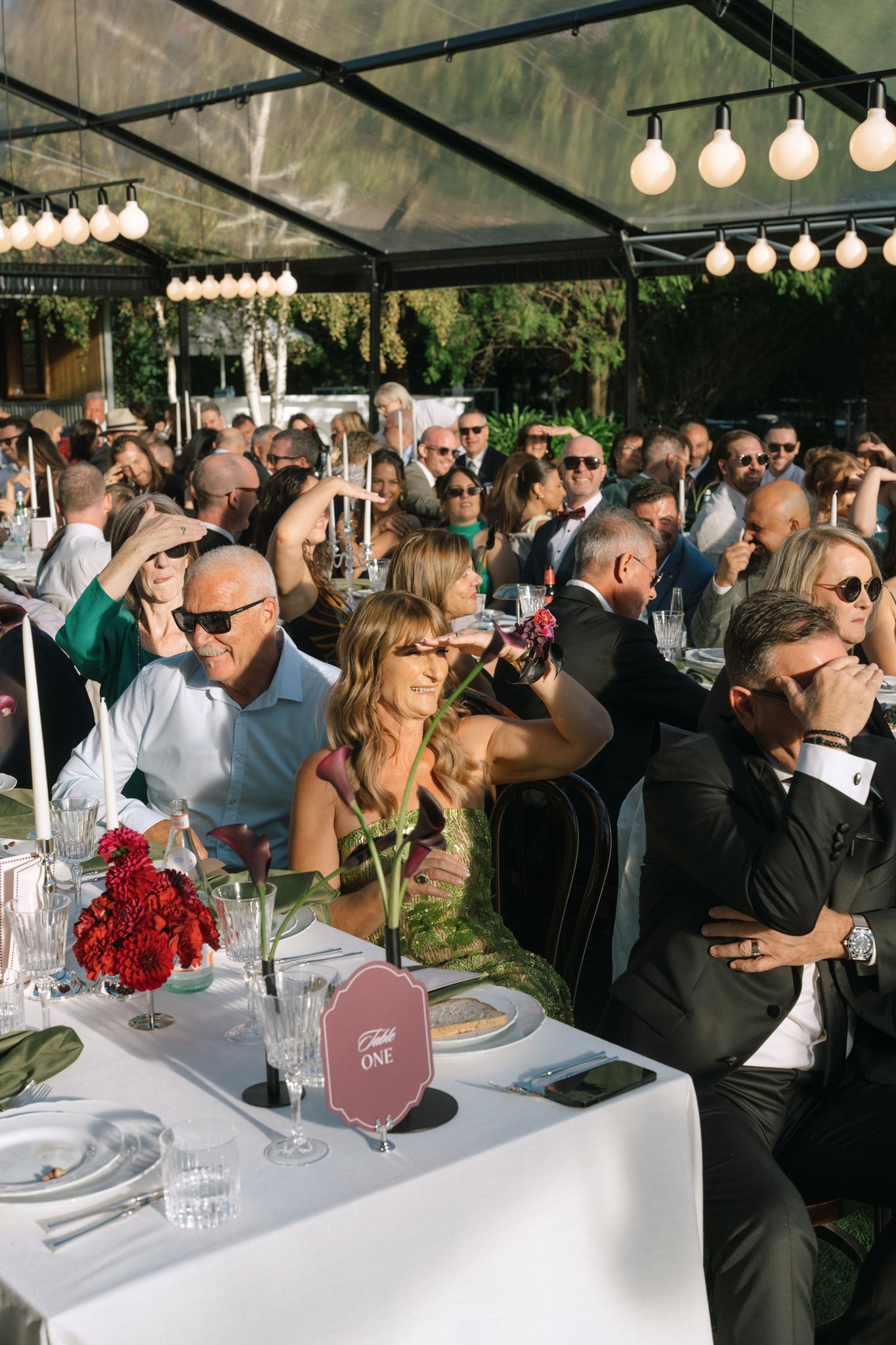 Weddin guests bathed in sunshine in clear roof marqee for wedding reception