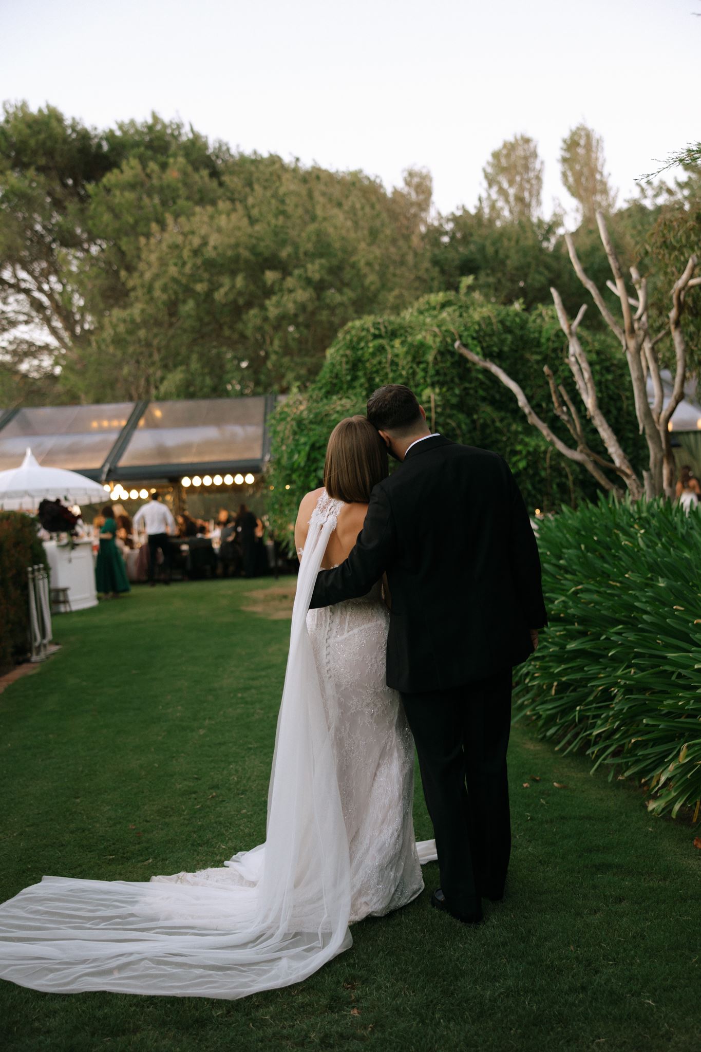Photograph of Bride and groom from behind, leaning into each other in garden at Whites Valley Estate
