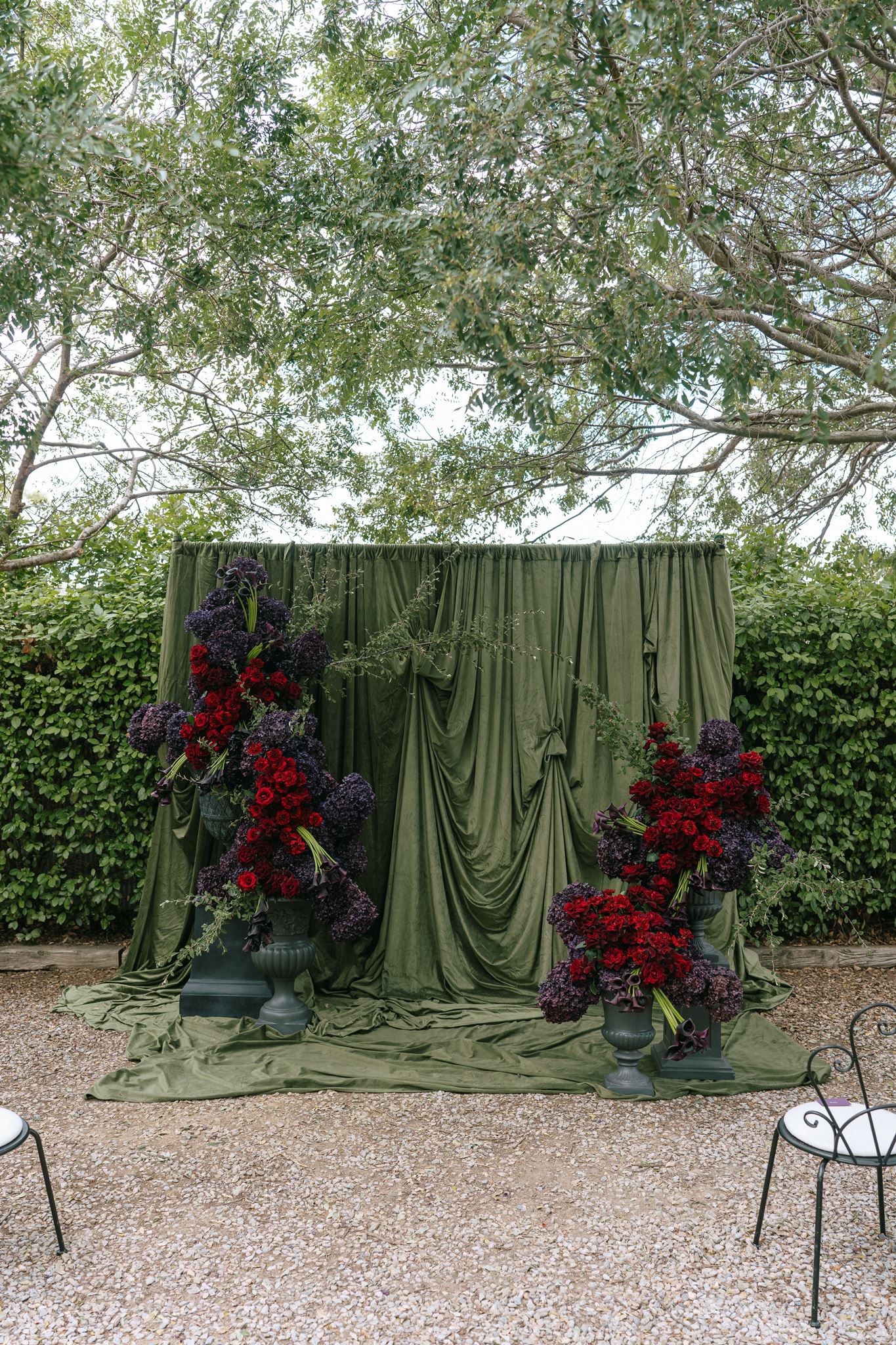 Dark green draped fabric wedding arbor with rich red and purple floral displays