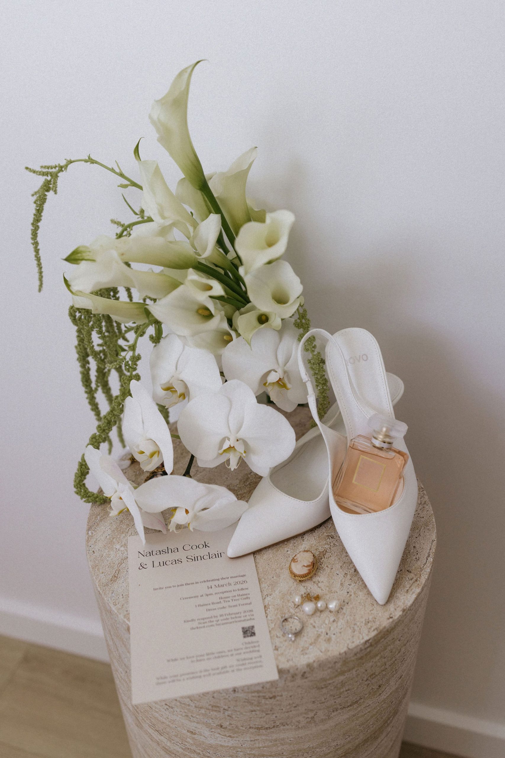 White wedding bouquet, bridal shoes and perfume on stone plinth