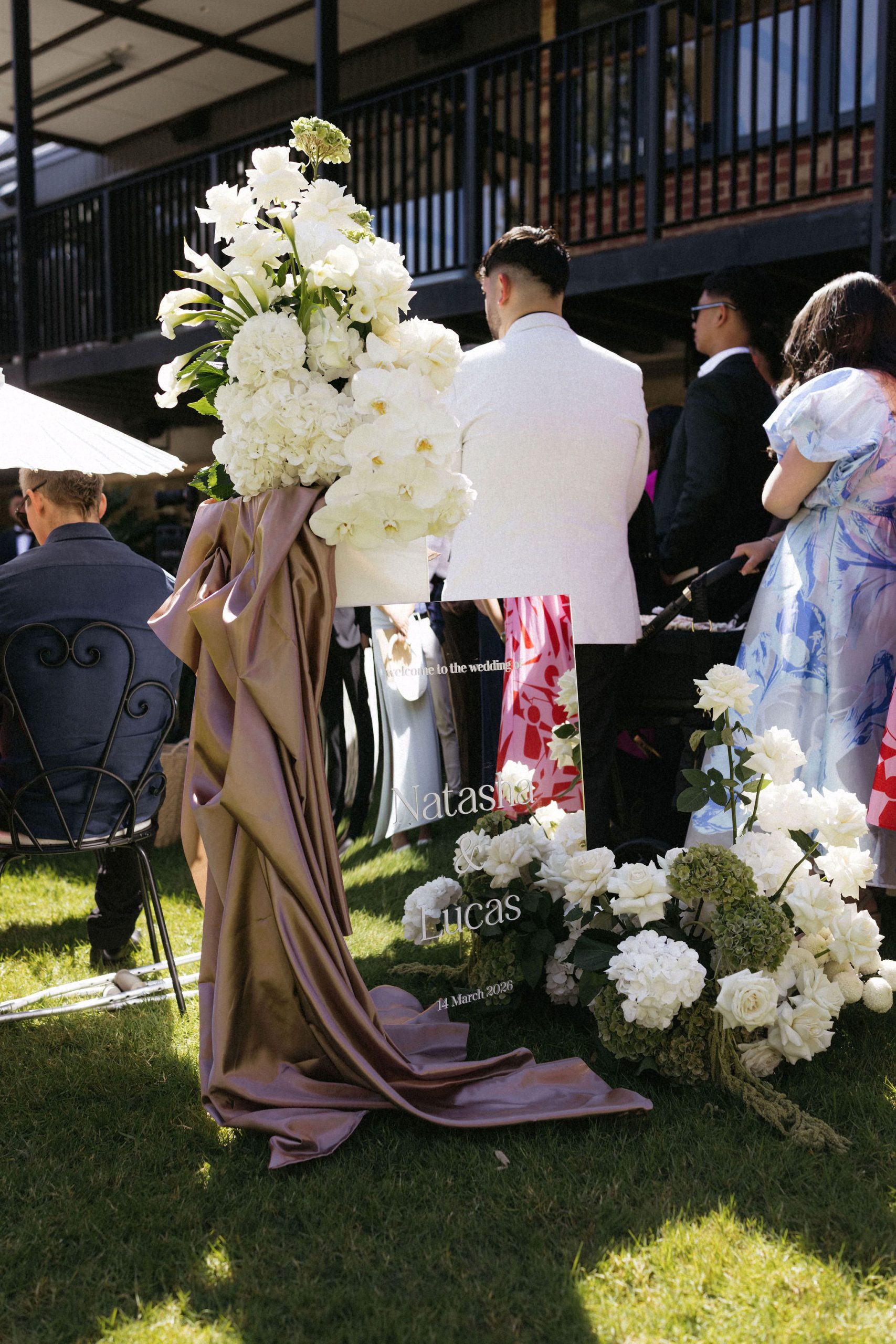 Mirror welcome sign sitting at top of aisle with draped silk and white and green floral displays
