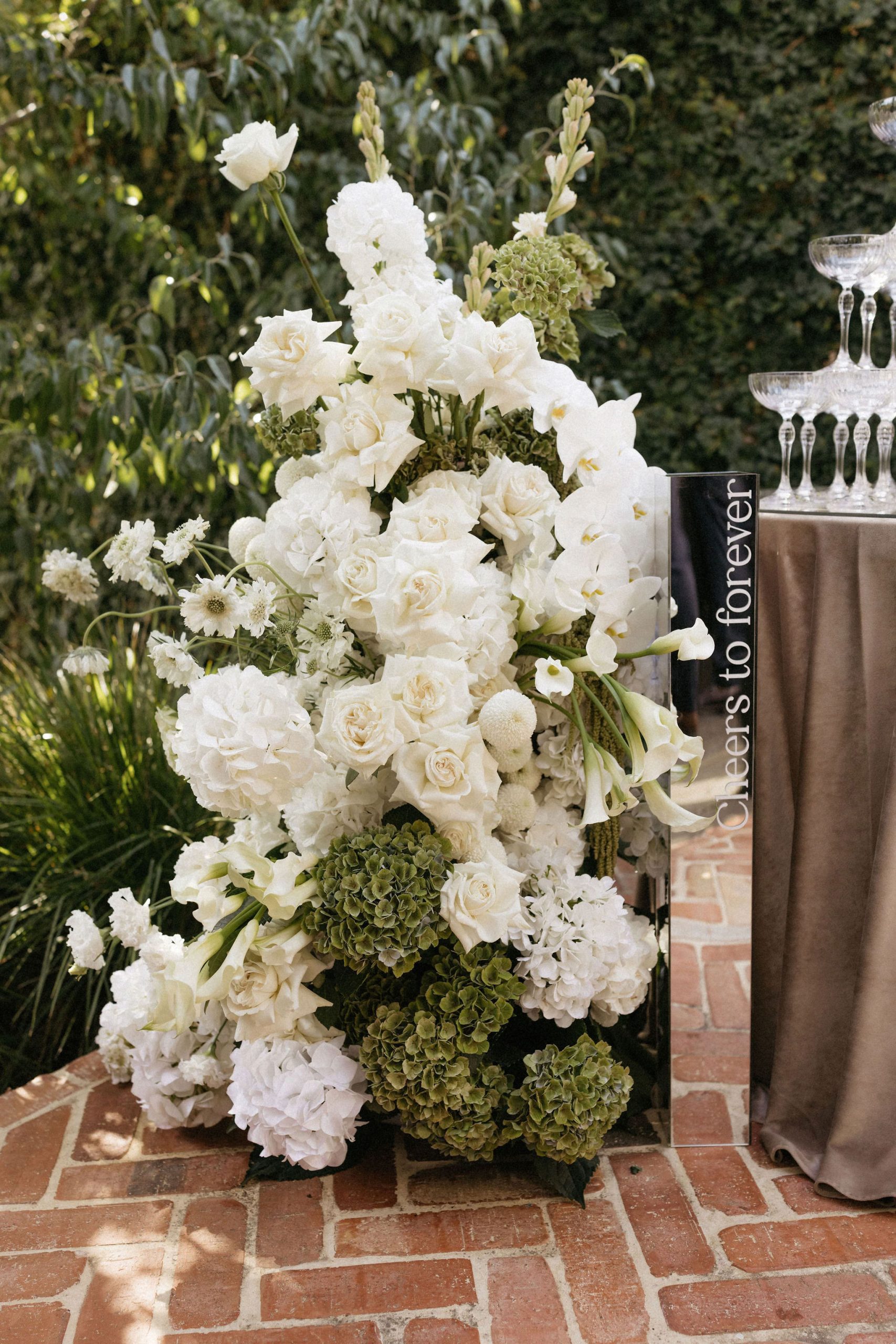 Large white and green floor floral arrangement and mirror plinth with writing "Cheers to forever"