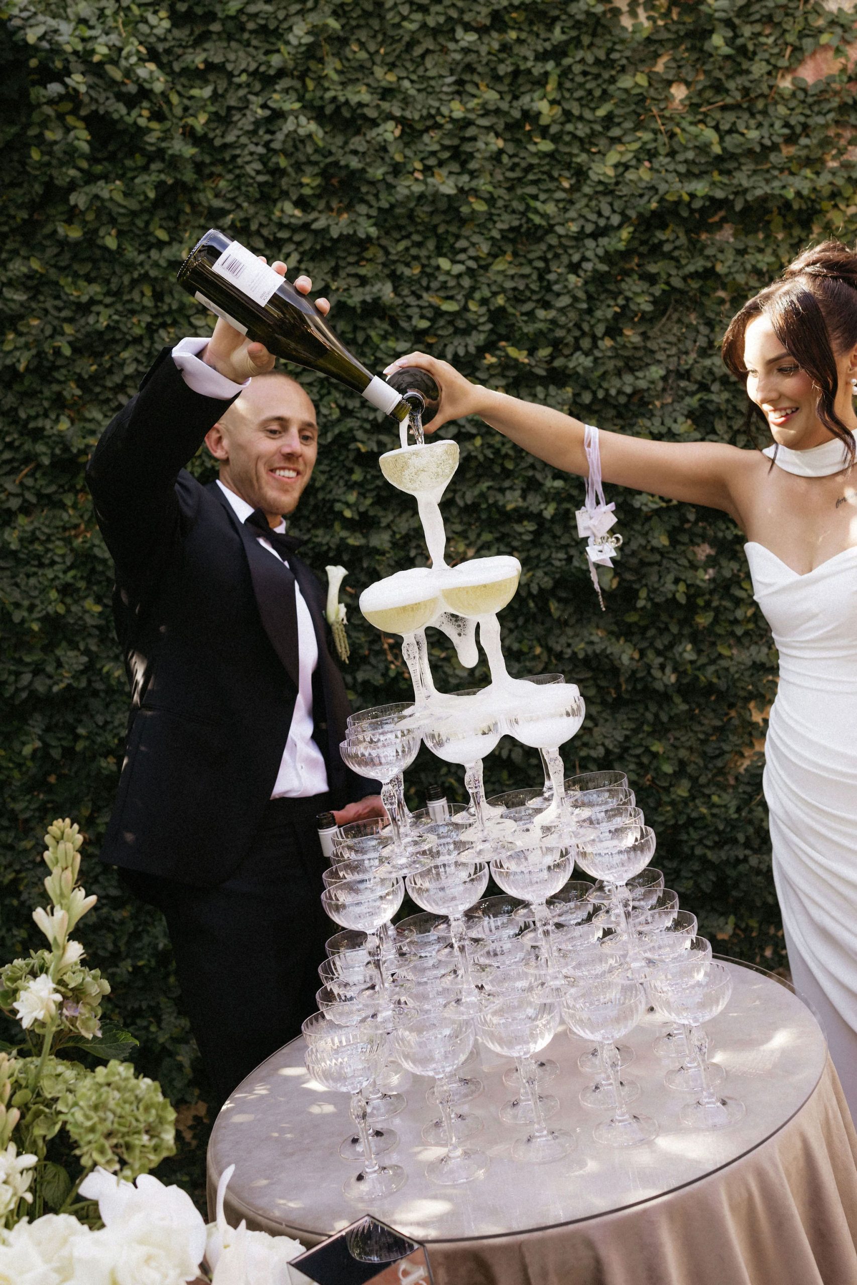 Bride and groom pouring champagne into champagne tower in garden at House on Haines styled by The Modern Approach