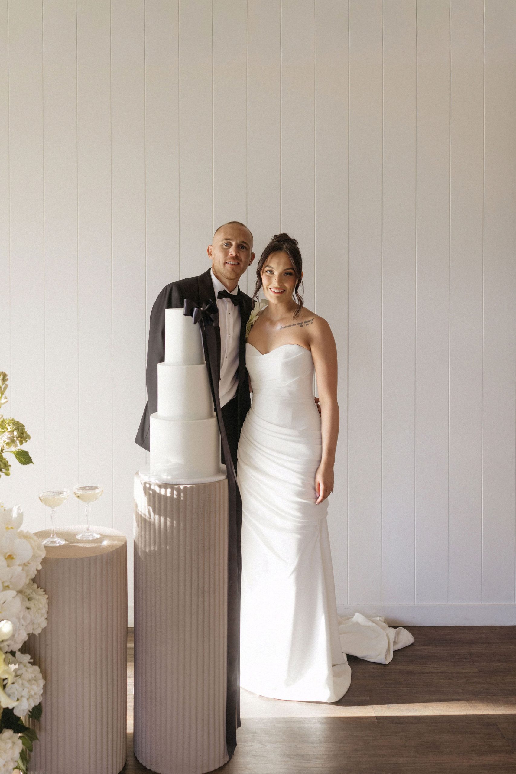 Bride and groom standing with modern white minimalist wedding cake on stone plinth