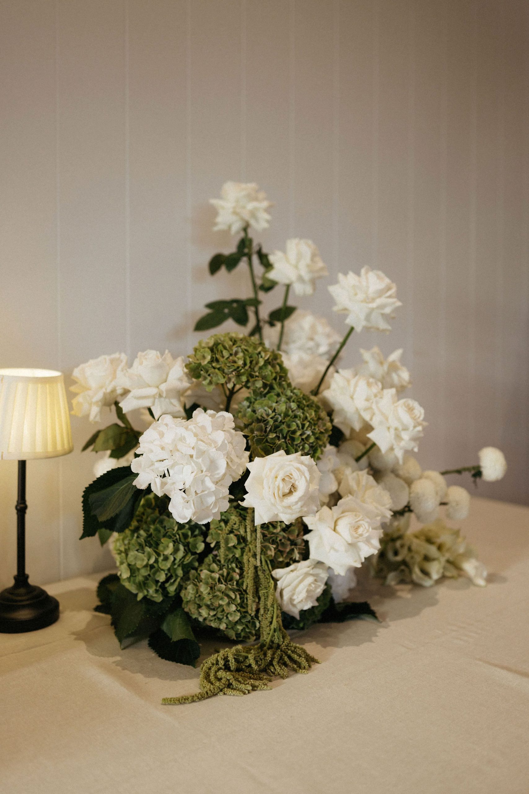 White and green Floral table arrangement next to lamp on linen tablecloth