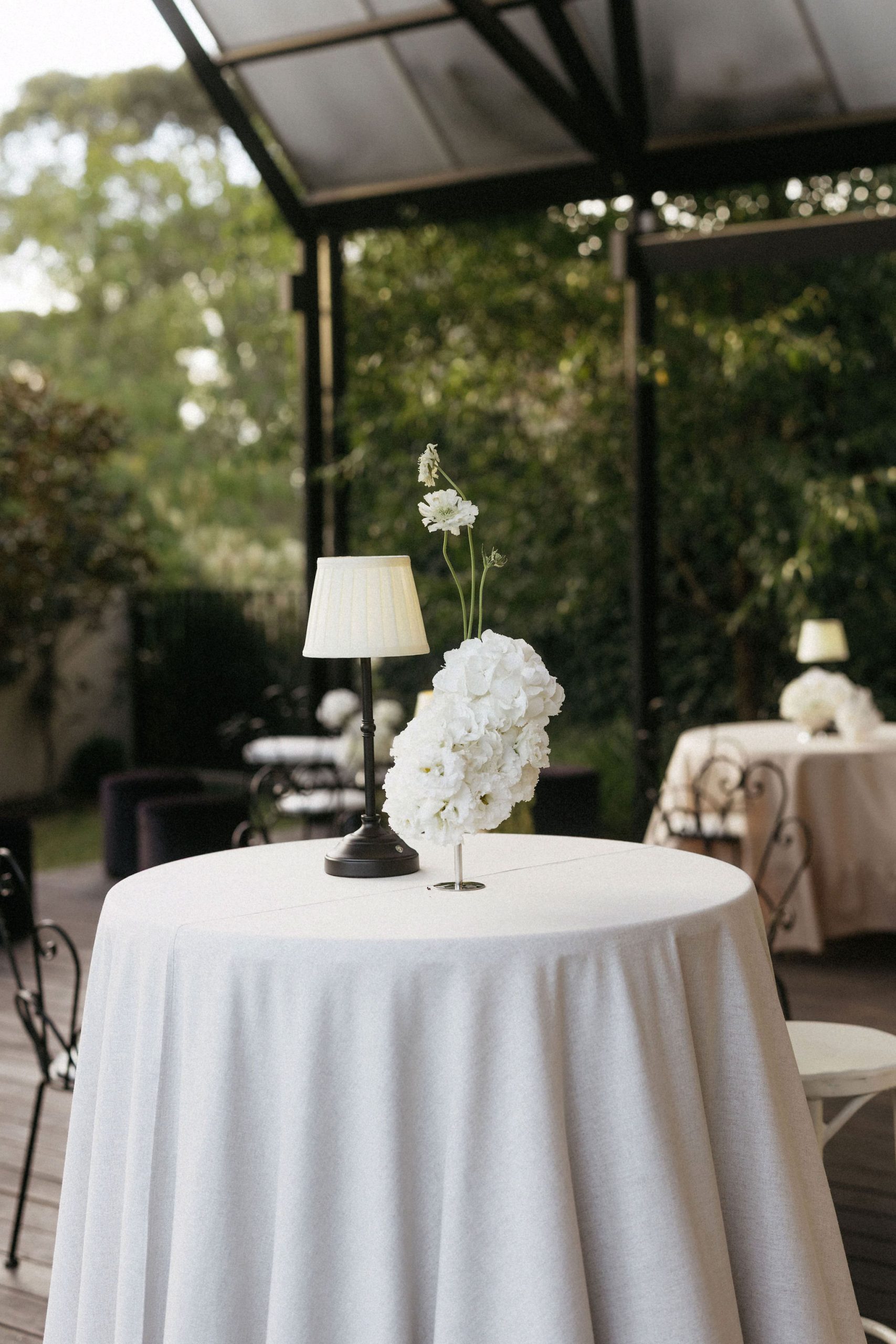 Small white floral arrangement and lamp on round wedding reception table at House on Haines